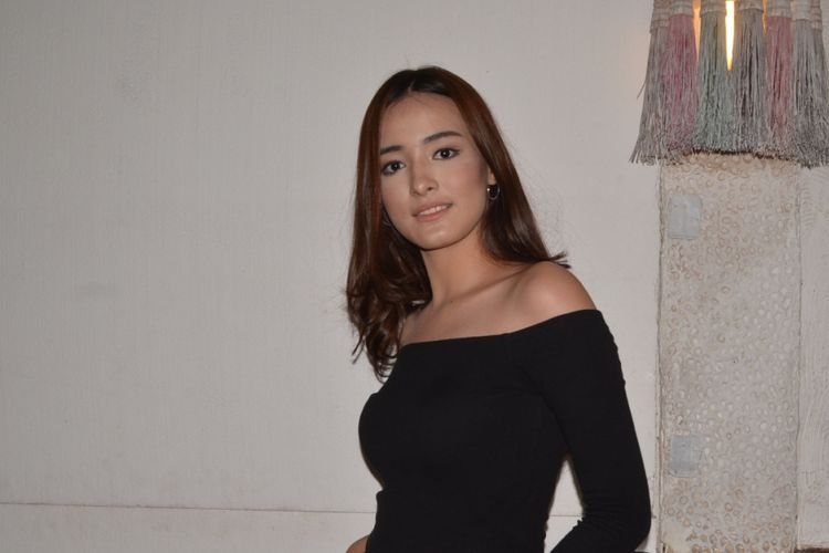 Mawar de Jongh mengenakan atasan off-shoulder hitam sambil berpose di depan dinding putih